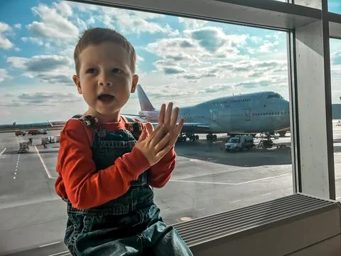 A small red-haired boy is waiting to board a flight in the airport transit ha Stock Photos
