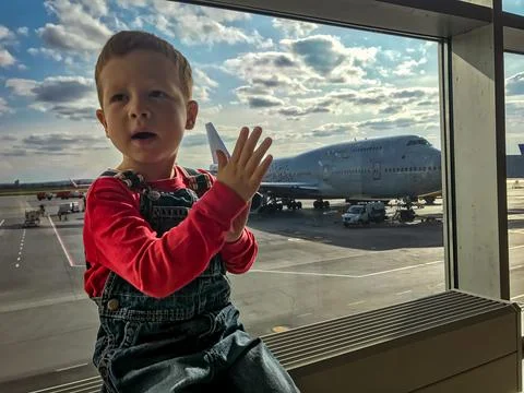 A small red-haired boy is waiting to board a flight in the airport transit ha Stock Photos
