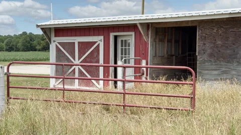Small red horse barn run-in shed with white cross beams stands behind rusty.. Stockbeeldmateriaal 337578417