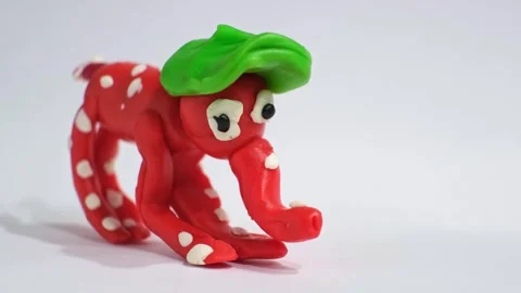 A small red plasticine elephant with white spots and a green hat stands in a Stock Footage 339340085