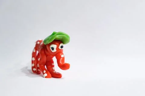 A small red plasticine elephant with white spots and a green hat stands in a Photos