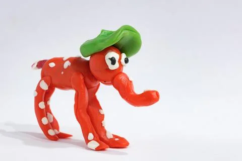 A small red plasticine elephant with white spots and a green hat stands in a Stock Photos