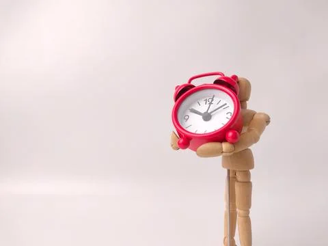 Small, red, retro-style analog alarm clock held by a wooden articulated man.. Stock Photos
