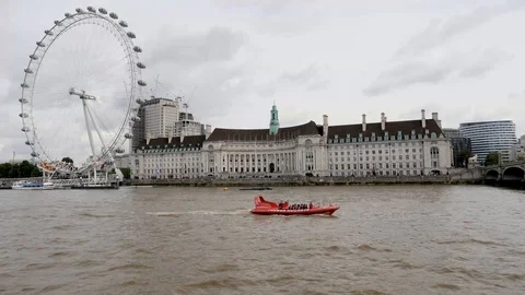 Small red river boat passing London Eye and County Hall on River Thames Stock Footage 95373853