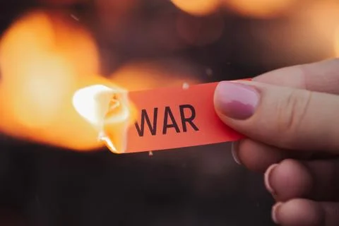 Small red sheet of paper in hand of a girl with burning word war on it, close up Stock Photos