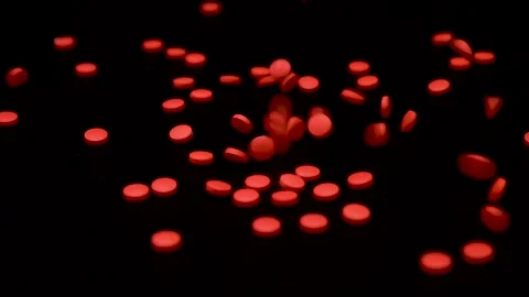 Small red tablets falling on a black surface in slow motion closeup Video stock 147550519