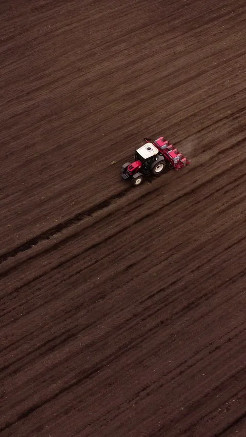 Small red tractor plowing soil in a field, showcasing the continuous motion of Stock Footage 325201678