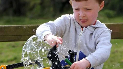 Small redhead boy playing and puddling in water a the garden Stock Photos