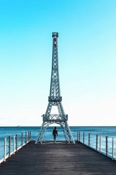 A small replica of the Eiffel tower on the beach. A lonely girl looks at the Stock Photos