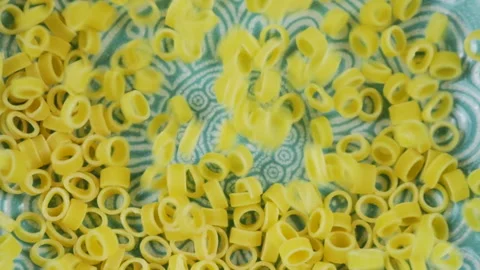 Small ring-shaped pasta is poured into a blue ceramic bowl. Top view. Slowmo Video stock 304742349
