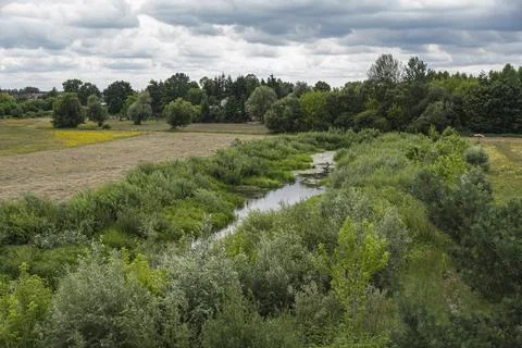Small river between meadows during cloudy day Stock Photos