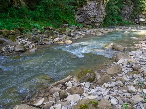 Small river flowing rapidly and vividly through its wild stony valley Stock Photos
