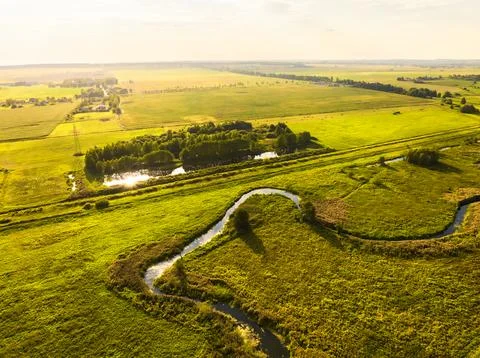 Small river flows among fields illuminated by sunset light Stock Photos