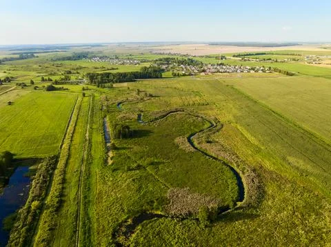 Small river flows among fields illuminated by sunset light Stock Photos