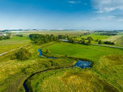 Small river flows among fields illuminated by sunset light Stock Photos