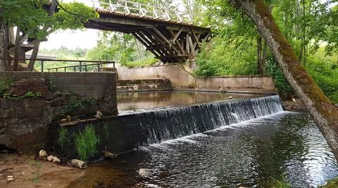 On small river there is an artificial waterfall under wooden bridge in the fo Stock Photos