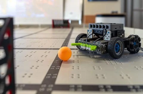 A small robot navigates a table while targeting an orange ball in a tech work 스톡 사진