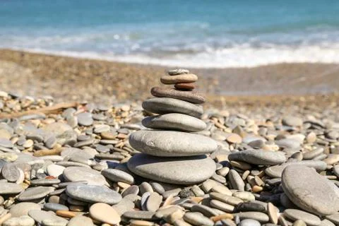 Small rocks layered to create a zen shape on a pebble beach with small waves Stock Photos