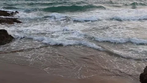 A small rocky beach with waves that roll into the sandy shore Stock Footage 153998494