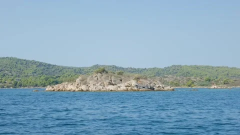 Small rocky islet surrounded by clear blue water, with the lush, green, forested Stock Footage 346681906