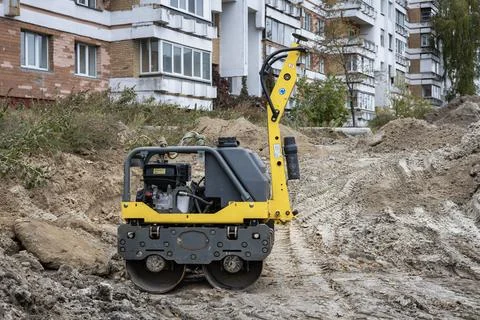 A small roller machine is at work on a construction site near residential bui 스톡 사진
