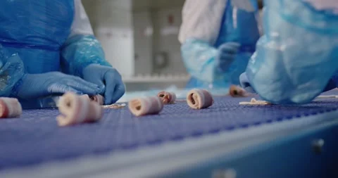 Small rolls of bacon on a blue conveyor belt checked by workers in protective Vídeo Stock 339993479