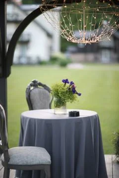 A small round table with a tablecloth and soft chairs stands under a canopy o Stock Photos