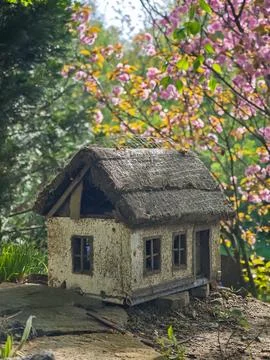 Small rustic miniature house with thatched roof in spring garden Stock Photos