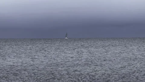 Small sailboat alone in the ocean under threatening storm clouds Video stock 293740172