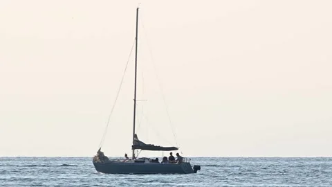 Small sailing boat passing by on open sea with people on board Stock Footage 138266361