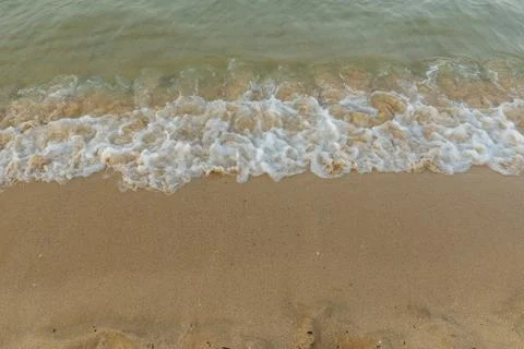 Small sea waves breaking on sandy beach in soft sunset light Stock Photos