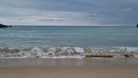Small sea waves gently washing sandy shore under cloudy sky Stock Footage 320134200