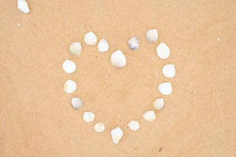 Small seashells in the shape of a heart on a smooth sandy beach. Stock Photos
