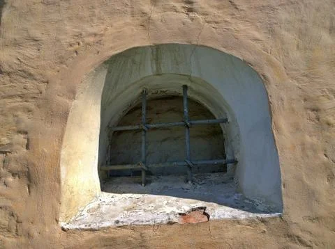 Small semicircular window in the old ancient stone wall with metal grill. Stock Photos
