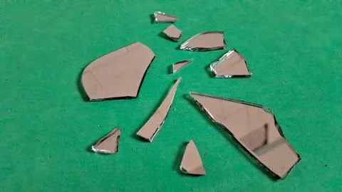 Small sharp shards of broken mirror on a vibrant green surface Stockfoto's