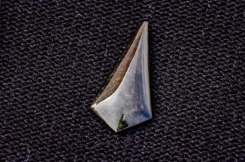 A small, shiny, triangular shaped stone is on a black surface 写真素材