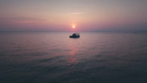 Small ship sailing across tranquil sea, surrounded by stunning pink and purple Stock Footage 312742260