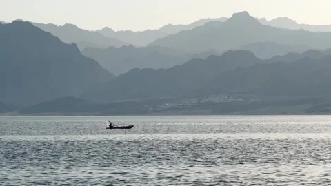 Small Silhouette of Man Rowing a Boat at Sea with Mountain layers on the Horizon Stock Footage 340943626