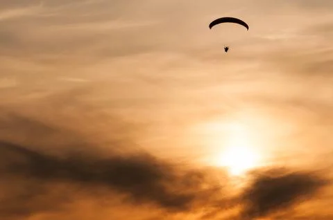 Small silhouette of a paramotor in flight at sunset Photos