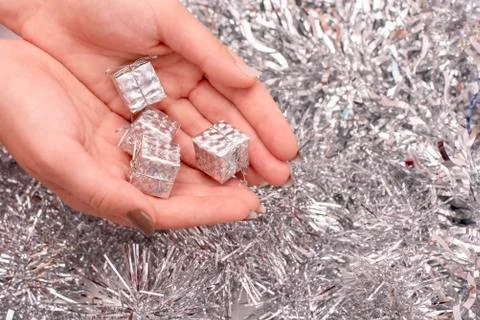 Small silver gift box in hand on background of tinsel Stock Photos