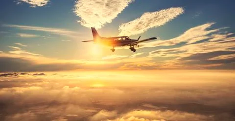 Small single engine airplane flying in the gorgeous sunset sky through the sea 스톡 사진
