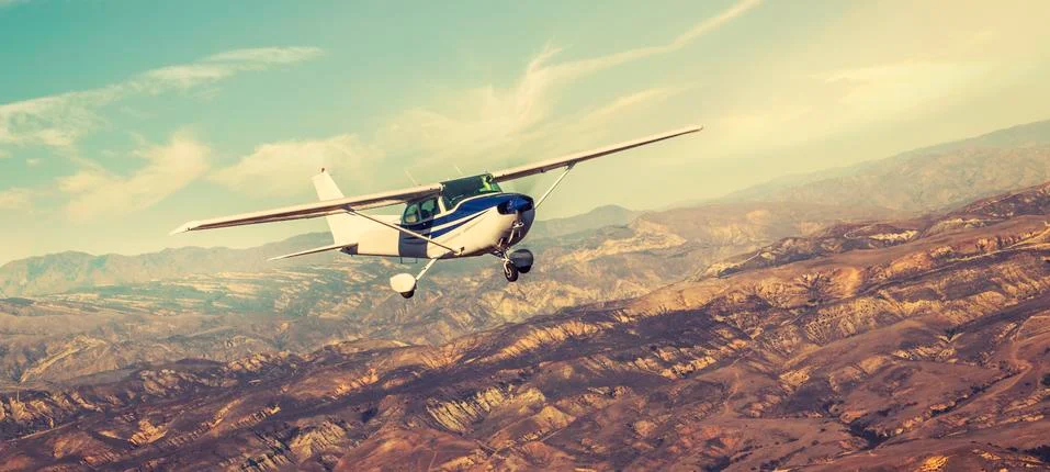 Small single engine airplane flying in the gorgeous sunset sky through the sea Stock-Fotos