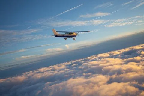 Small single engine airplane flying in the gorgeous sunset sky through the sea Fotos de archivo