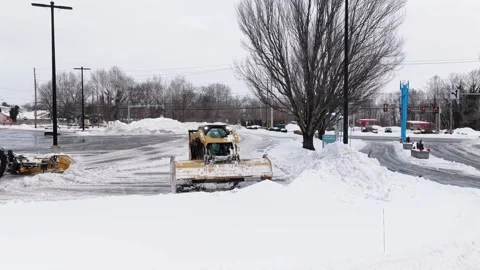 Small skid steer loader clearing snow in shopping center parking lot after Stock-Footage 332124399