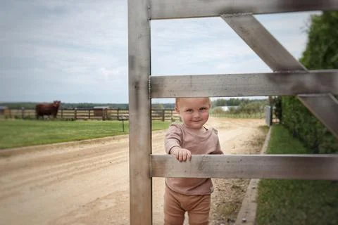 A small smiling boy in beige clothes is standing near the fence Stock Photos