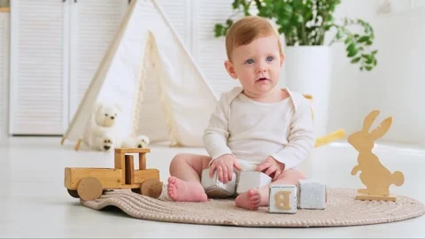 A small smiling child, a boy in a white bodysuit, plays with wooden toys on a Stock Footage 277385533