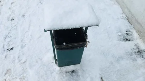 A small snow-covered trash can stands on the street in winter during a snowfall Stock Footage 295106856