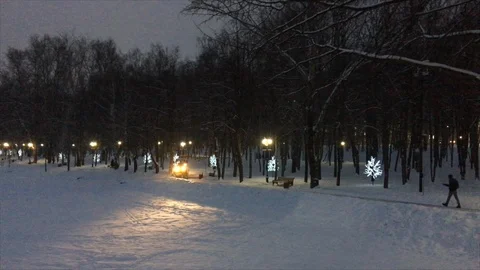 A small snow-removing tractor with headlights turned on cleans the footpath. Stock Footage 100231546
