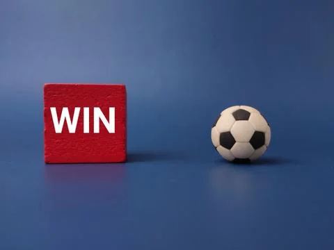 A small soccer ball sits on a solid blue surface next to a red wooden cube .. 库存照片