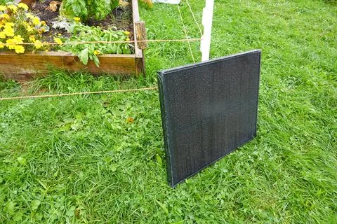 Small solar panel leaning on grass next to vegetable garden Stock Photos